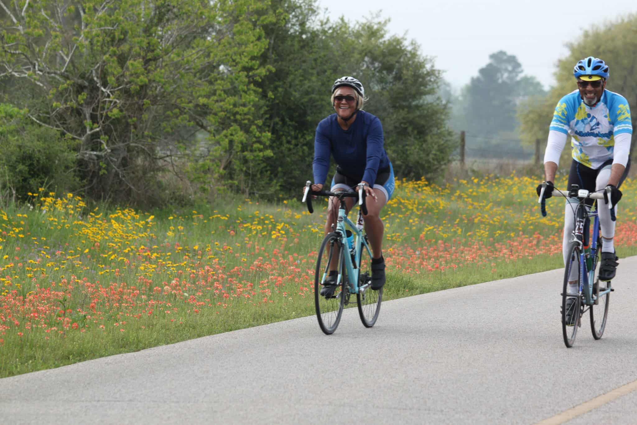 Brightly colored bicycles with smiling cyclists riding along a scenic trail surrounded by wildflowers and greenery.