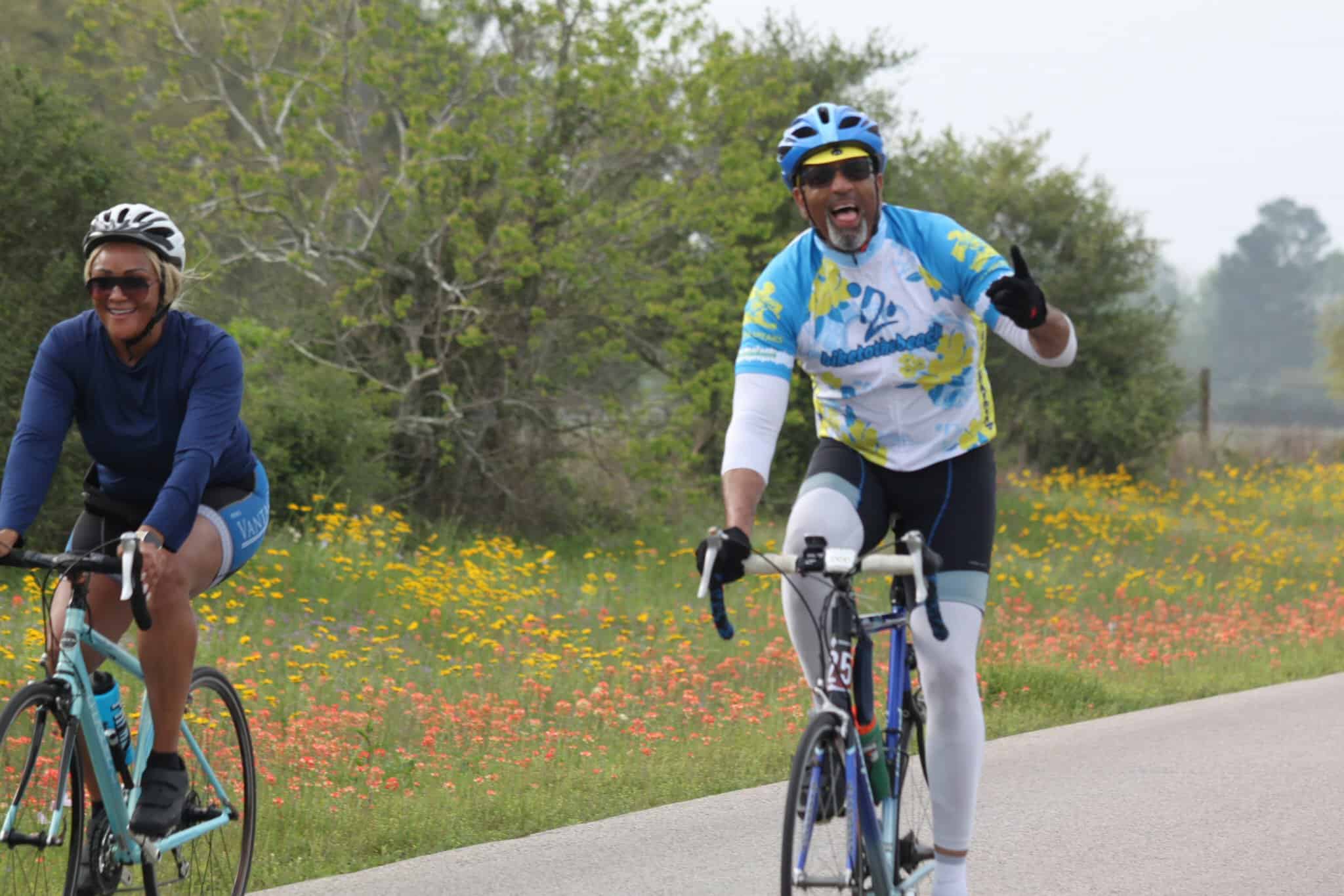Adult cycling enthusiasts enjoying the scenic Bluebonnet Express route with vibrant wildflowers in the background.