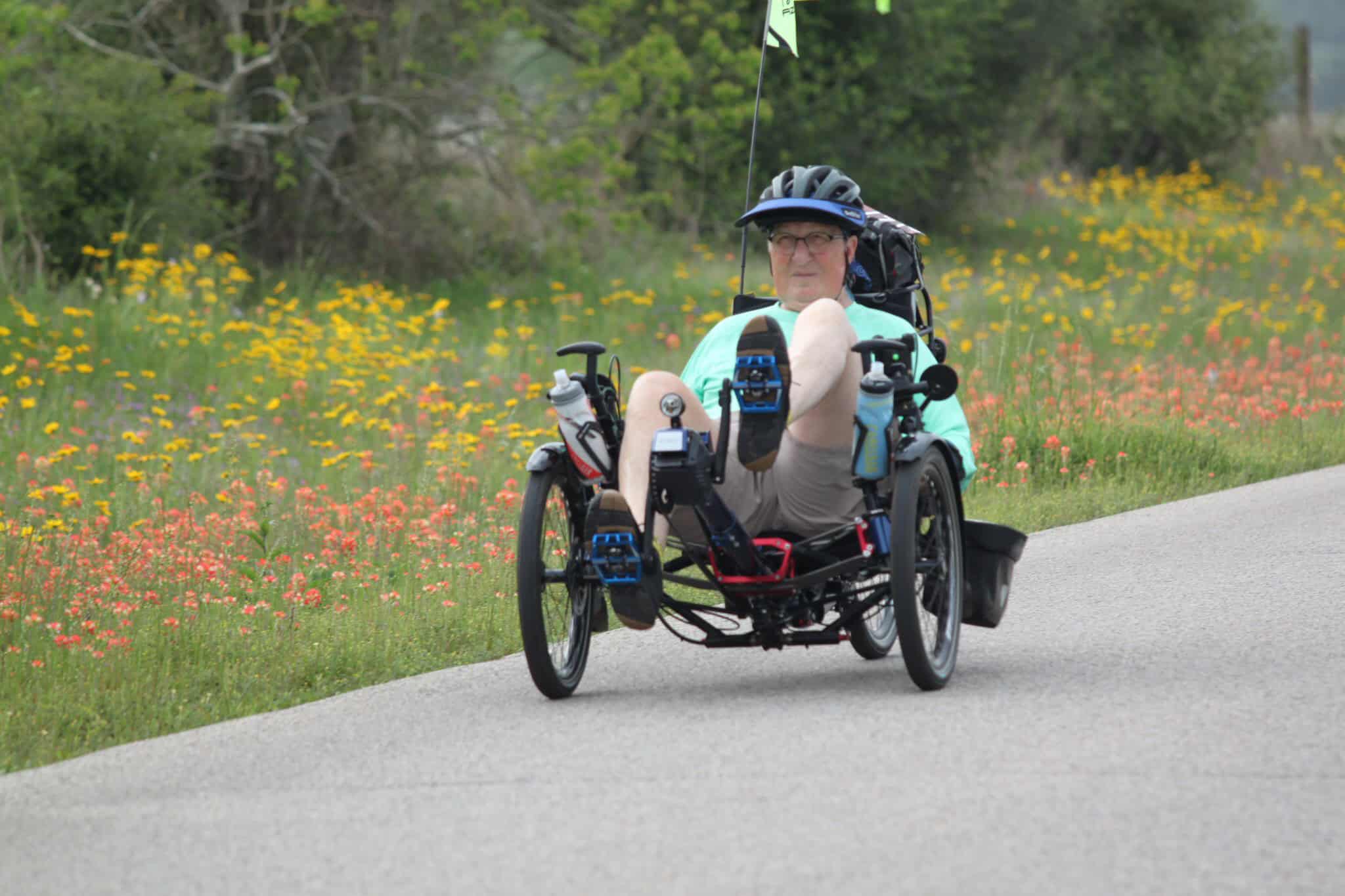 Handicap accessible recumbent bike riding through scenic wildflower landscape.