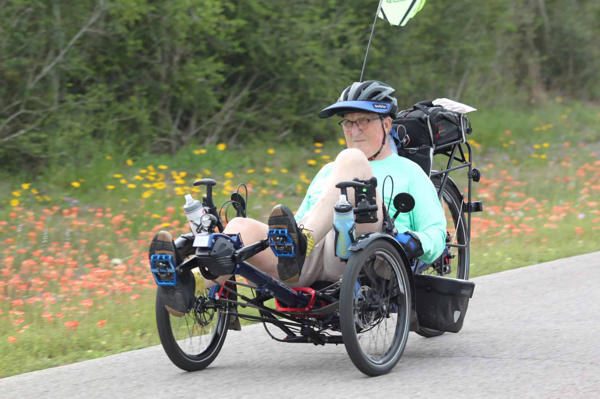 Allterrain electric wheelchair on scenic outdoor road with wildflowers and lush greenery.