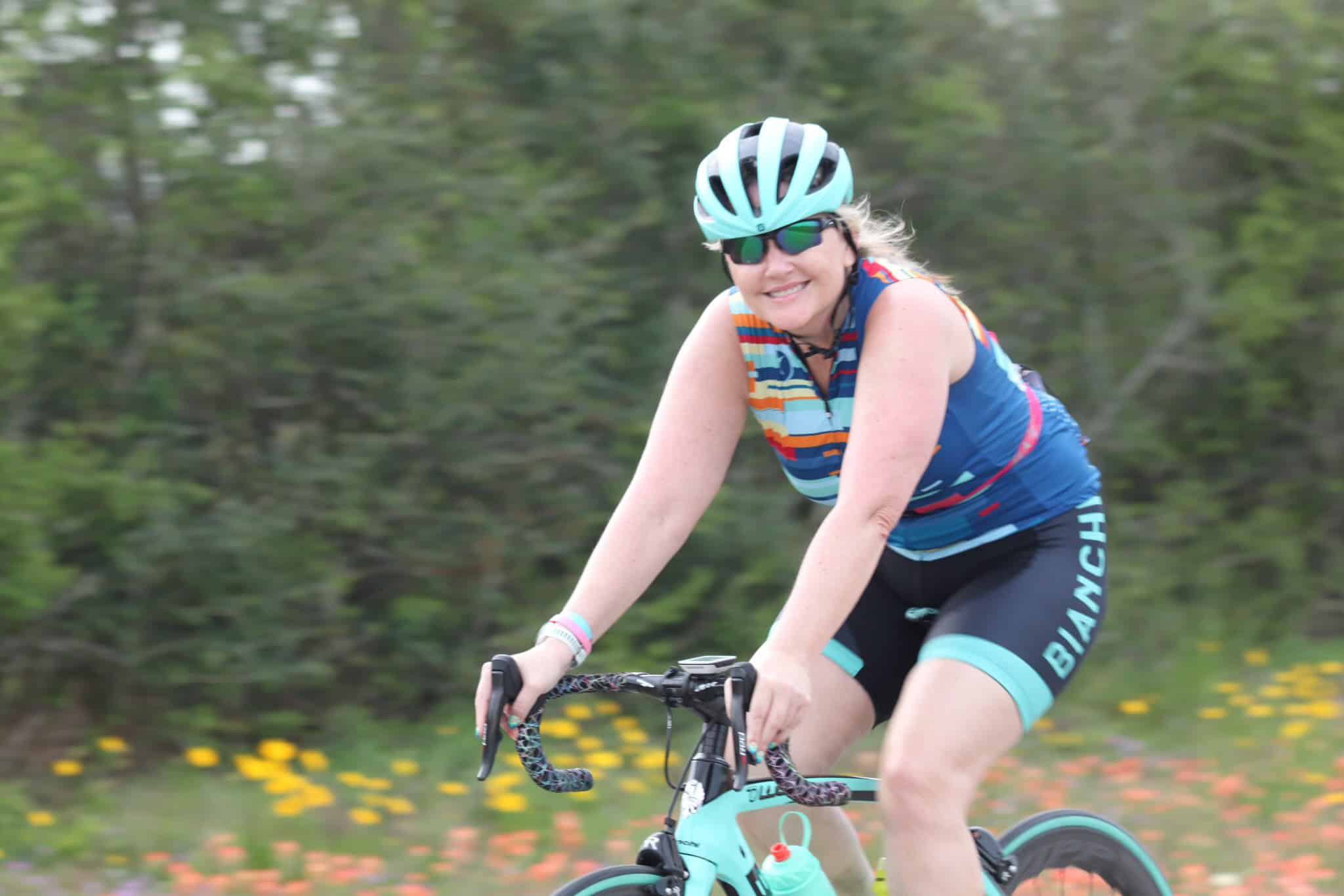 Bright female cyclist enjoying outdoor ride with Bluebonnet Express bike, surrounded by nature and colorful flowers.