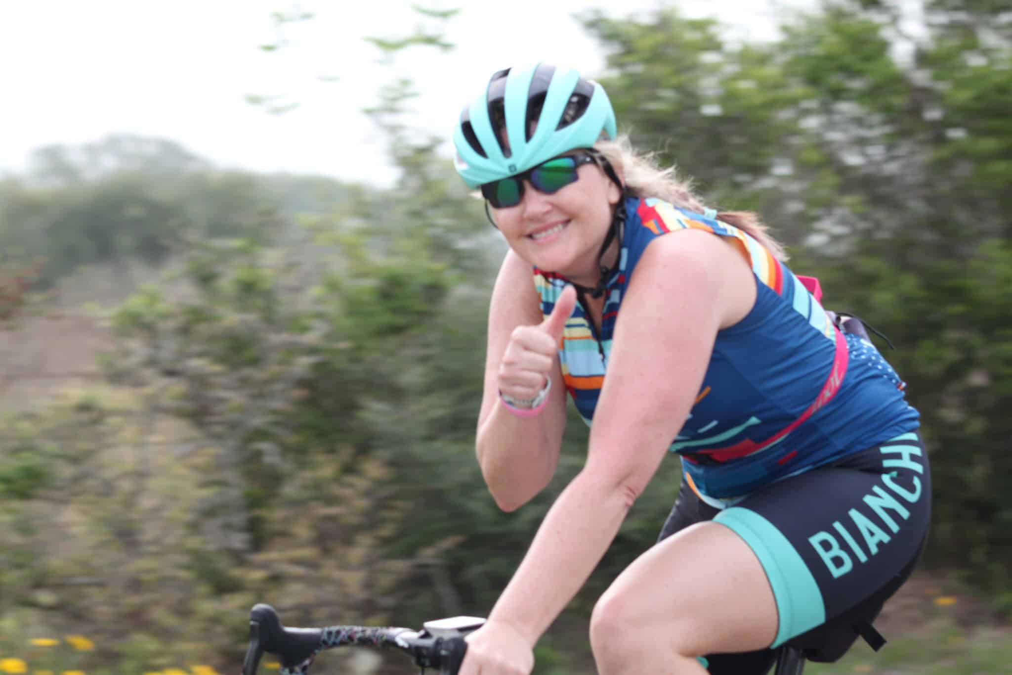 Cyclist wearing Bluebonnet Express gear giving a thumbs-up while riding outdoors.