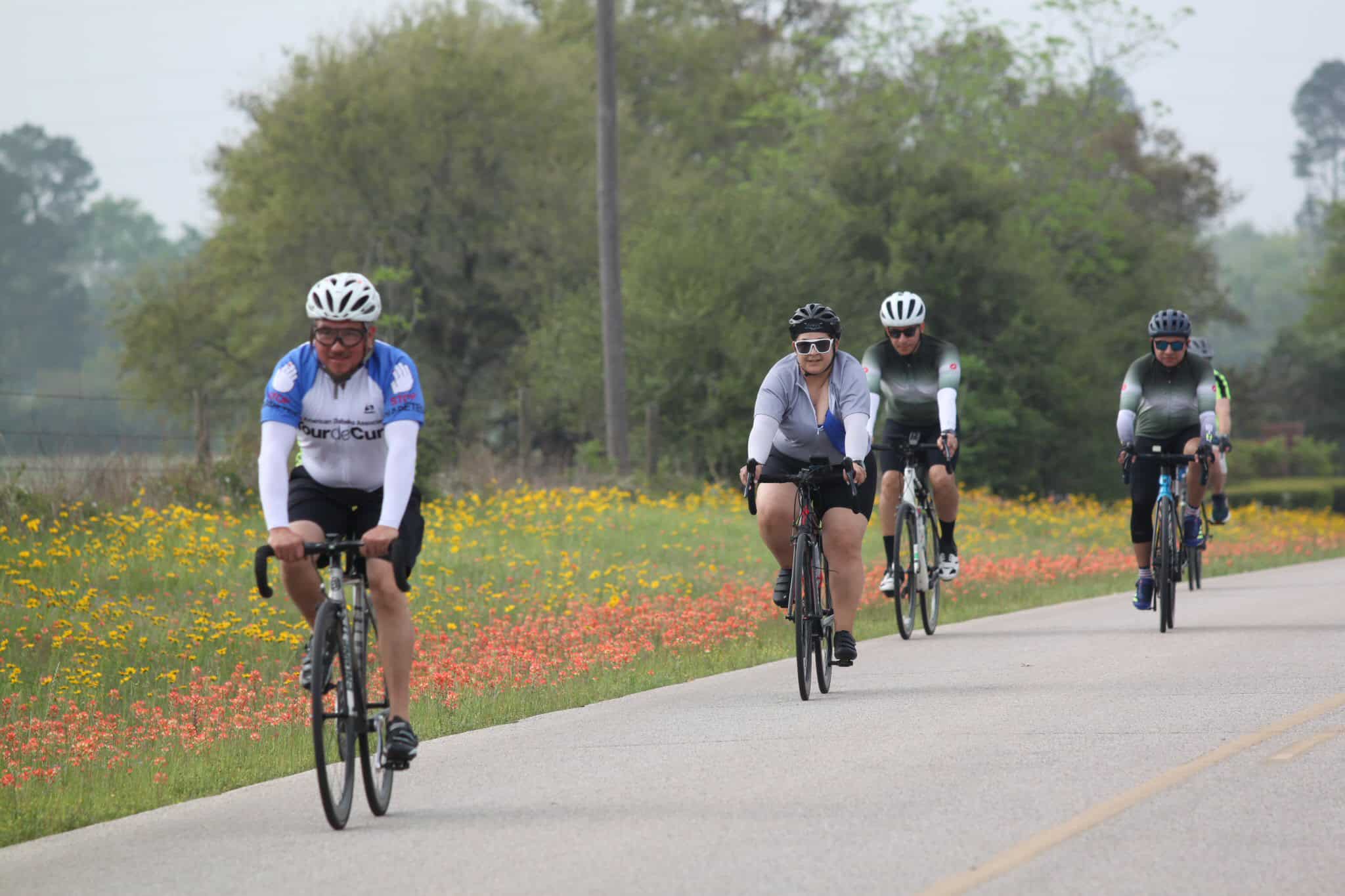Vibrant group of cyclists riding along scenic countryside route with blooming wildflowers.