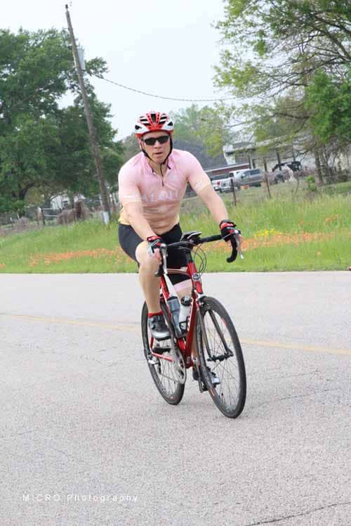 Rider in pink cycling jersey on Bluebonnet Express bike on rural road during daytime.