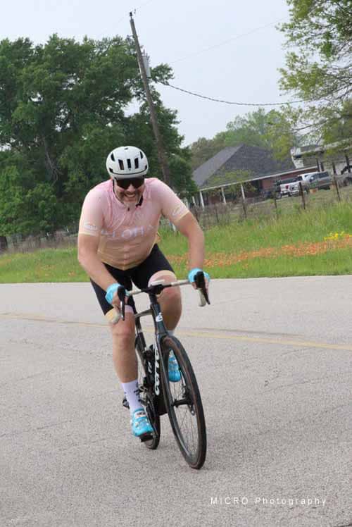 Bright cyclist riding Bluebonnet Express bike on rural road in Texas.