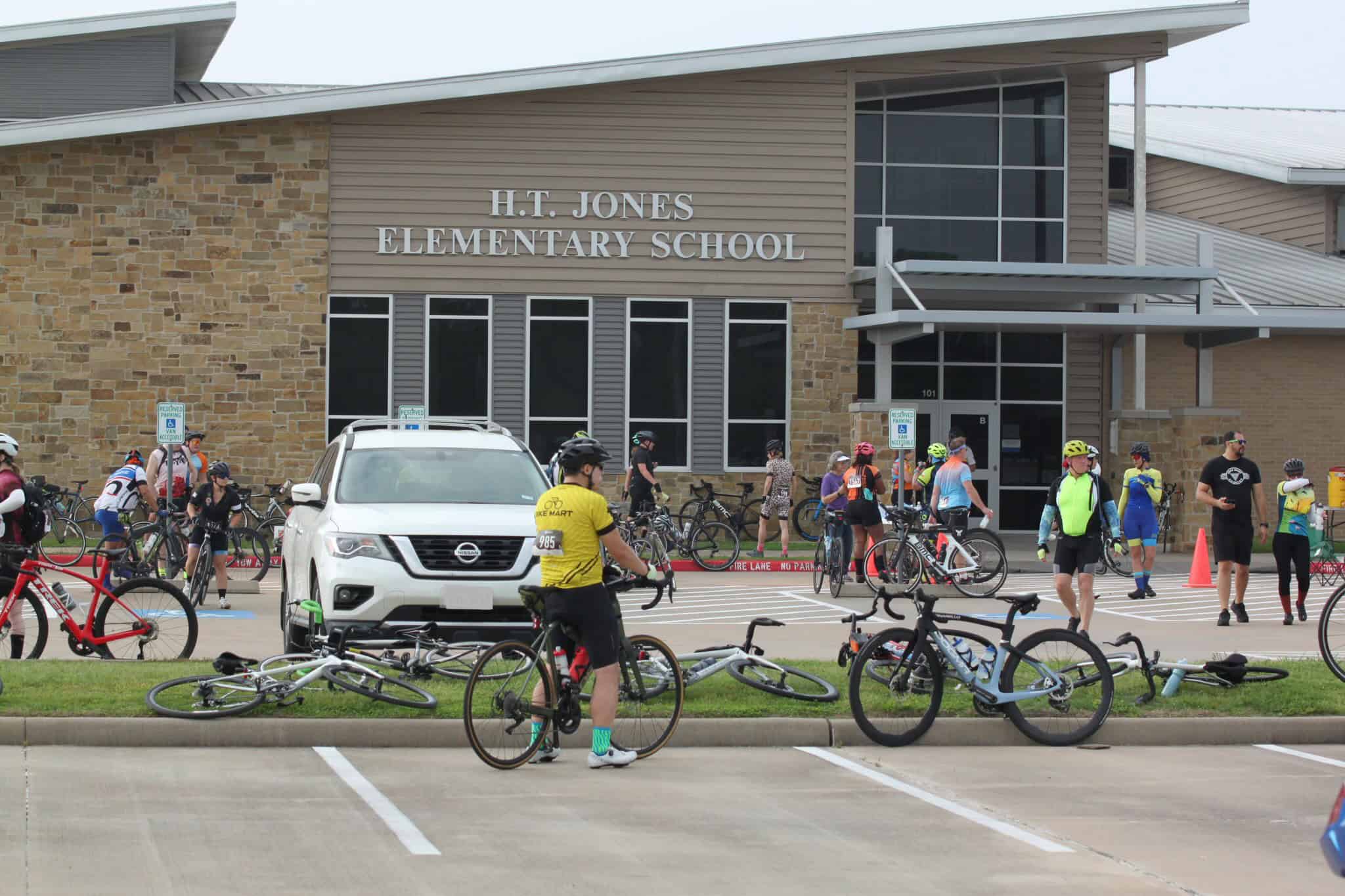 Bicycle riders gathering outside H.T. Jones Elementary School for a cycling event.
