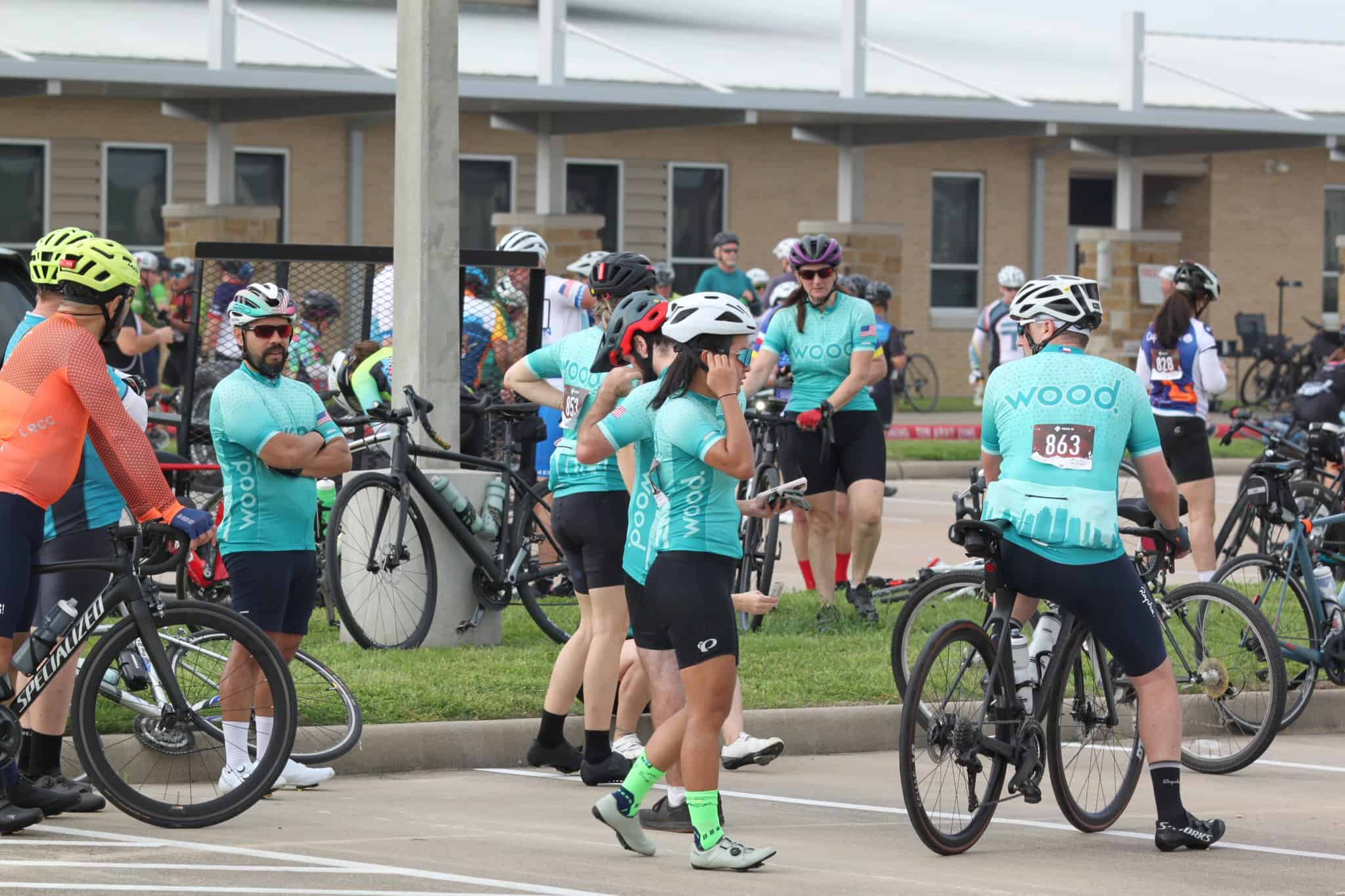 Cycling event participants with bikes in a parking lot, wearing branded jerseys and helmets.