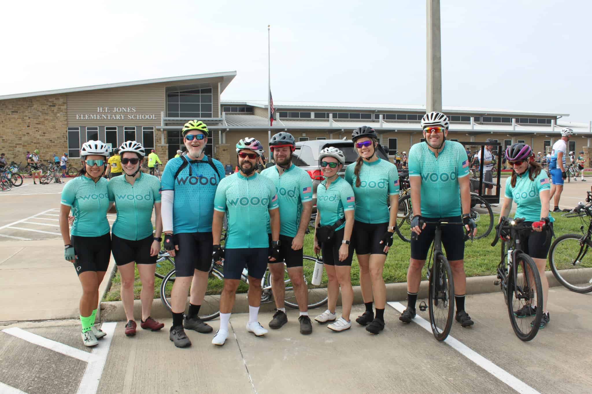 Cyclists in matching jerseys pose outside H.T. Jones Elementary School during Bluebonnet Express charity bike ride.