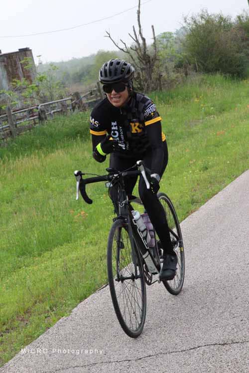 Cyclist riding on a scenic road with lush greenery, enjoying a Bluebonnet Express biking adventure.
