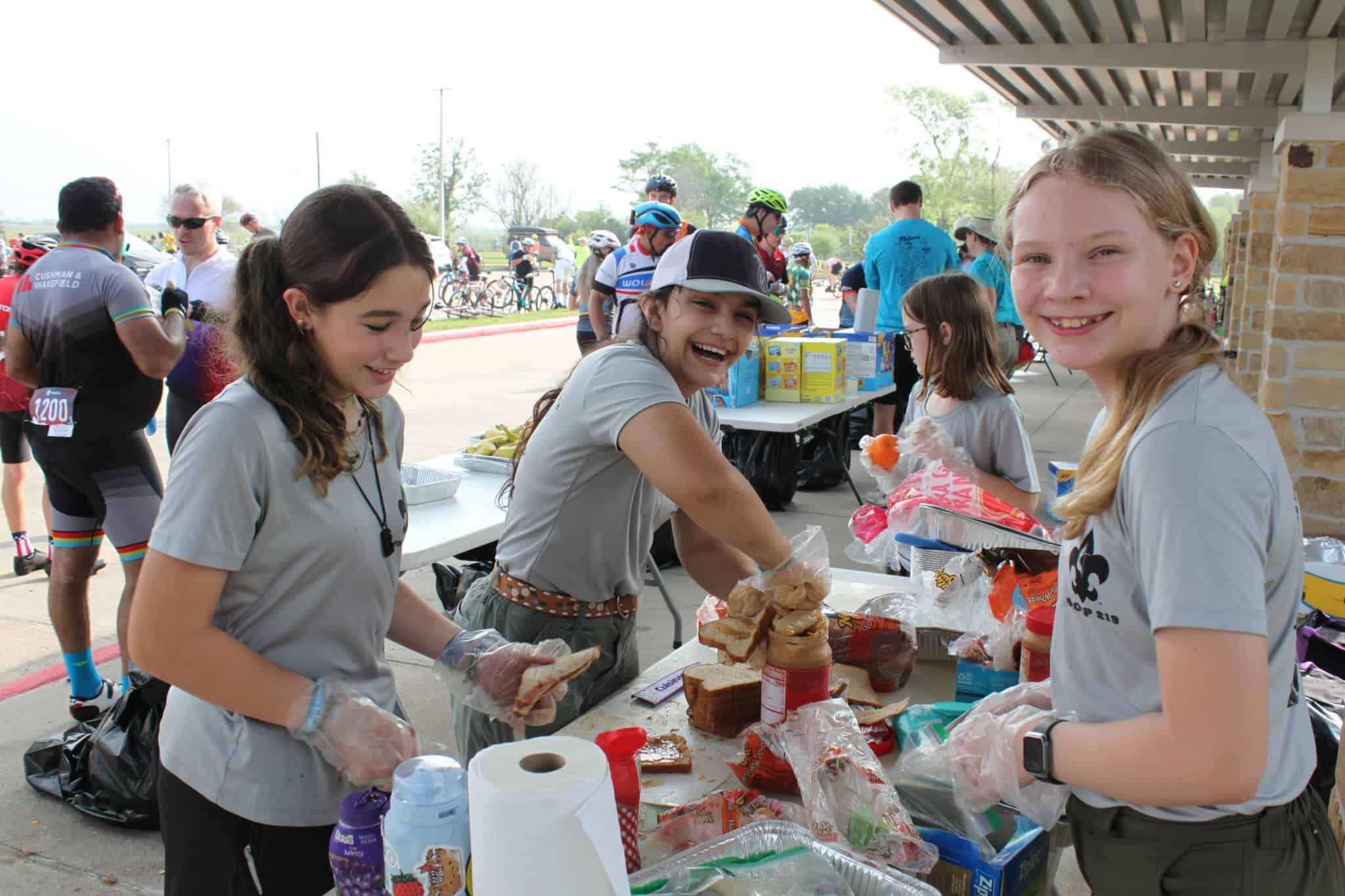 Smiling girls preparing sandwiches at Bluebonnet Express cycling event registration table.