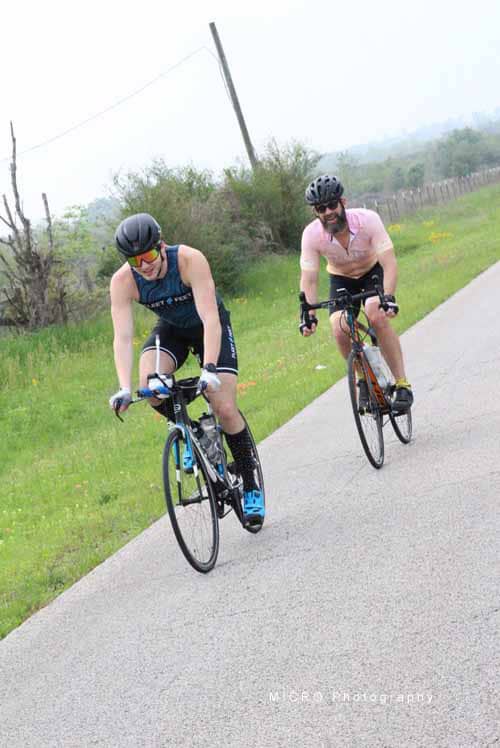 Two cyclists enjoying the Bluebonnet Express bike ride on a peaceful countryside road, promoting outdoor fun and fitness.