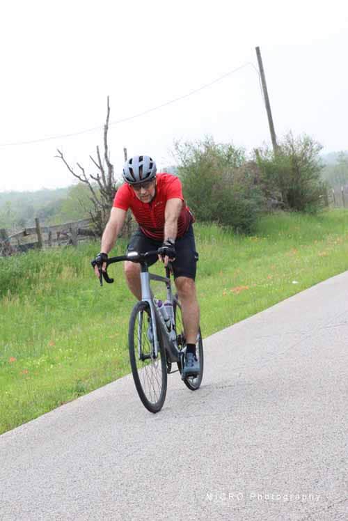 Vast cycling outdoors on scenic countryside road with rider wearing red helmet and jersey.