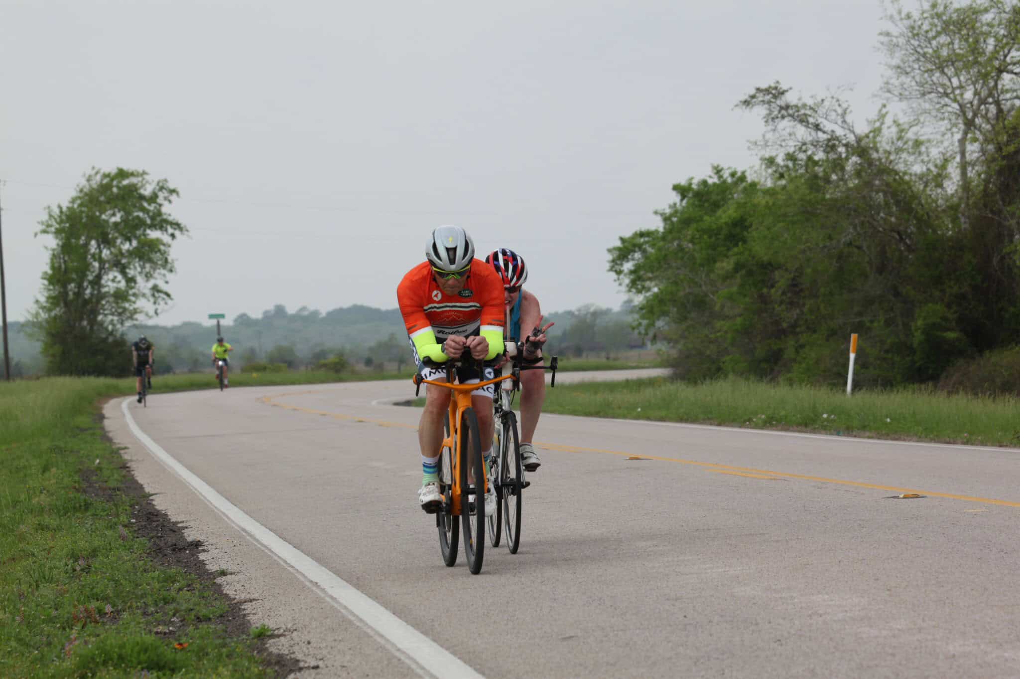 Vibrant cyclists on a scenic rural road with lush greenery, highlighting Bluebonnet Express cycling tour.