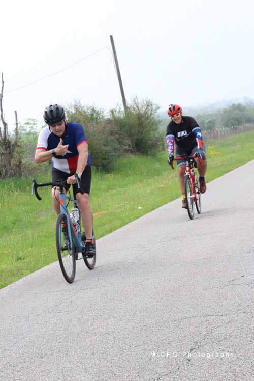 Bicycle riders on scenic rural road during daytime athletic cycling event.