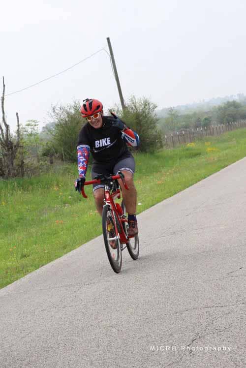 Brightly dressed cyclist riding on rural road with lush greenery, promoting Bluebonnet Express biking events and outdoor fitness.