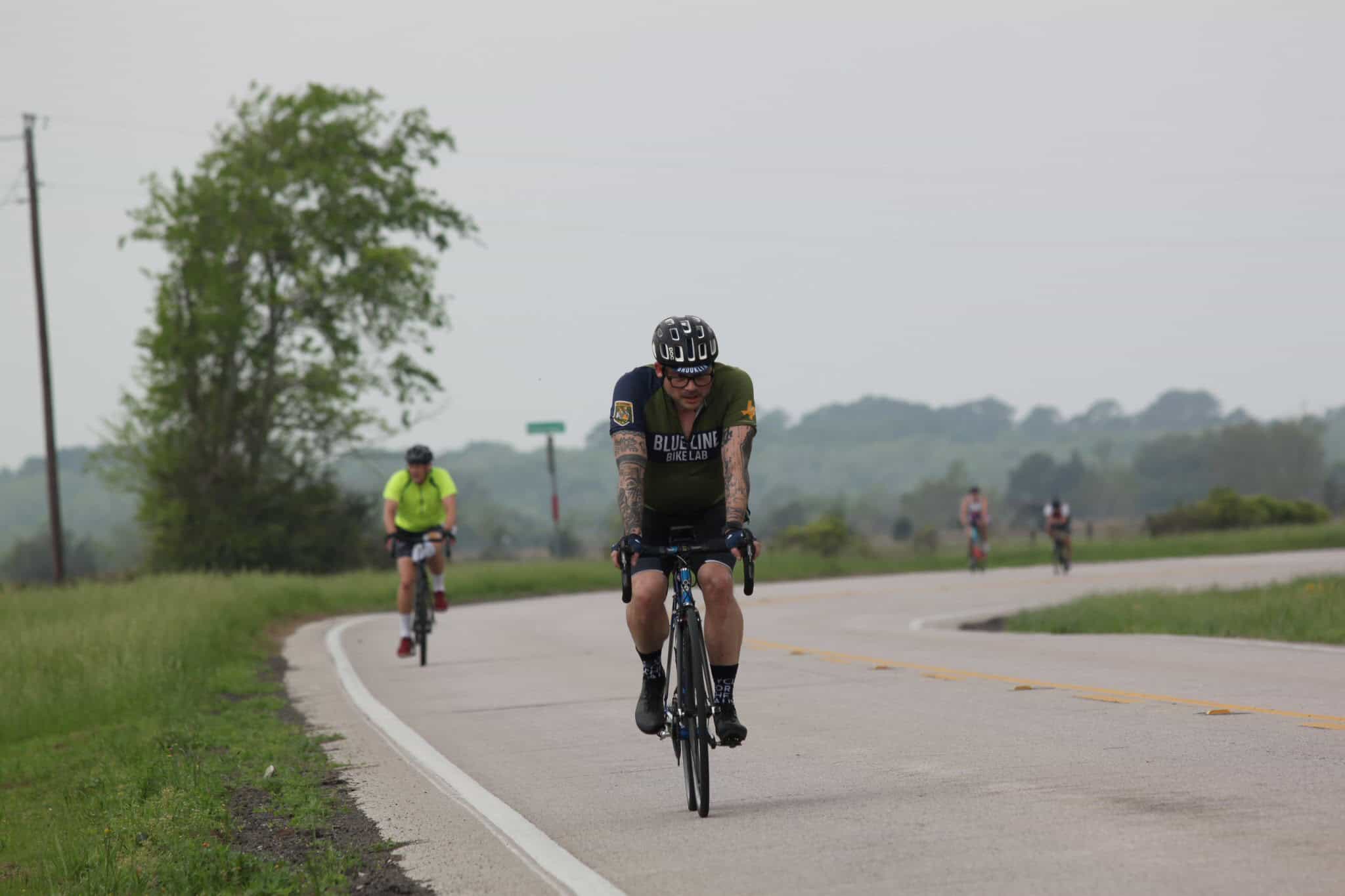 Bicycle rider in Bluebonnet Express cycling event on scenic rural road with cyclists in the background.
