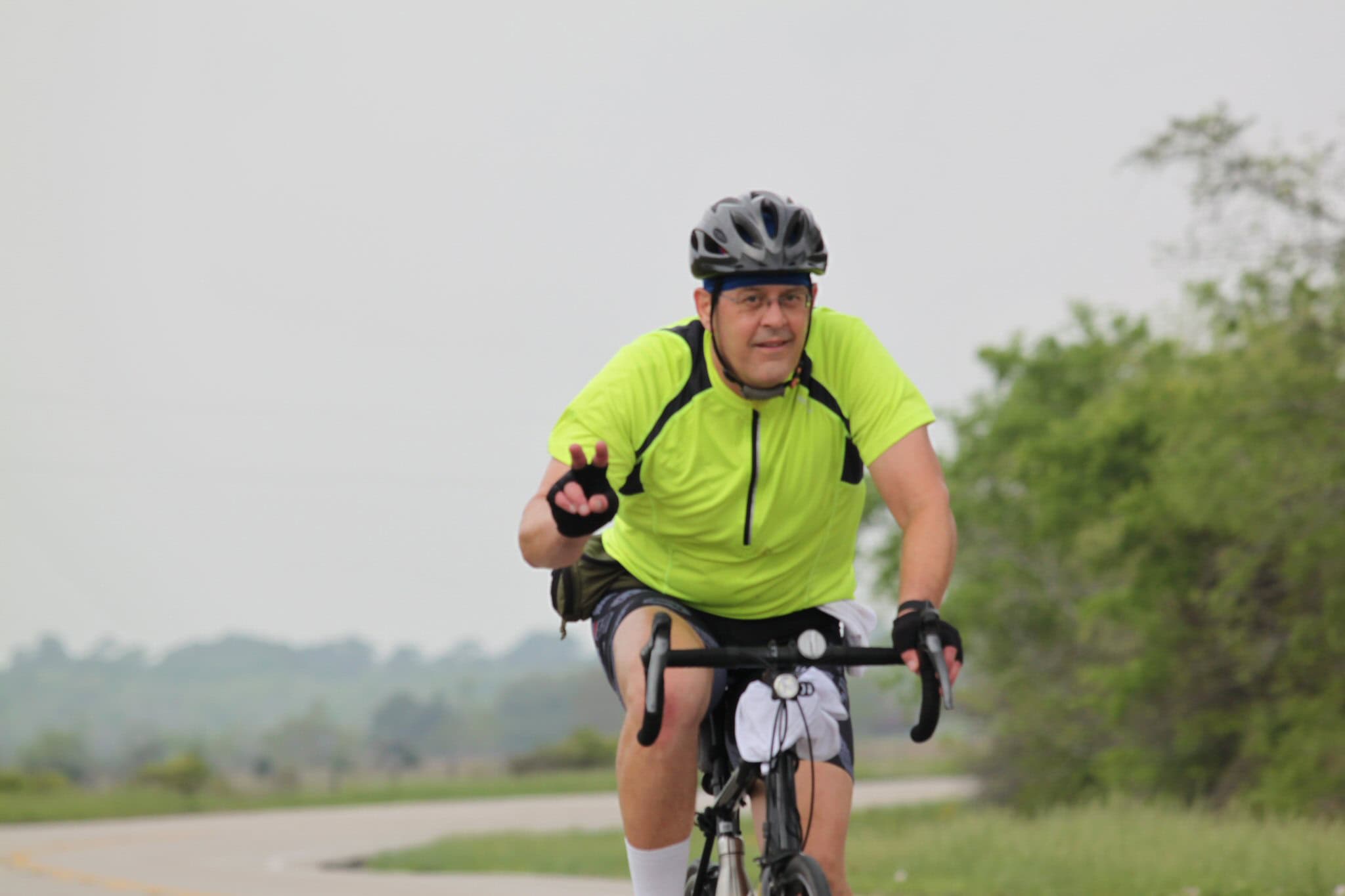 Vibrant cyclist wearing a neon yellow shirt riding a bike outdoors.