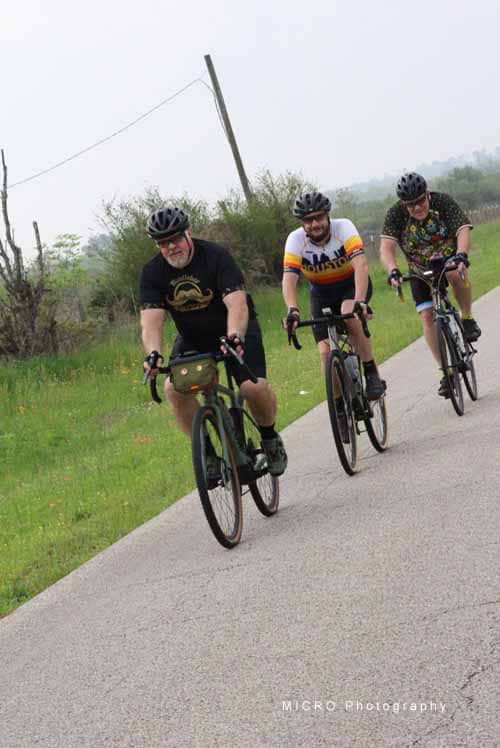 1. Group of cyclists riding on scenic rural bike trail with greenery and overcast sky.