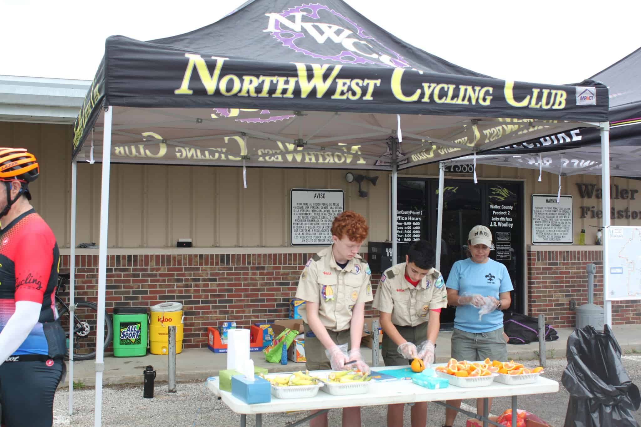 Vibrant North West Cycling Club tent at local event with volunteers preparing refreshments for cyclists.
