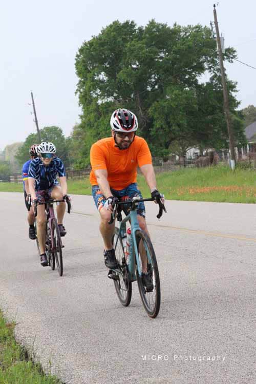 Brightly dressed cyclists riding on scenic rural road during daytime.