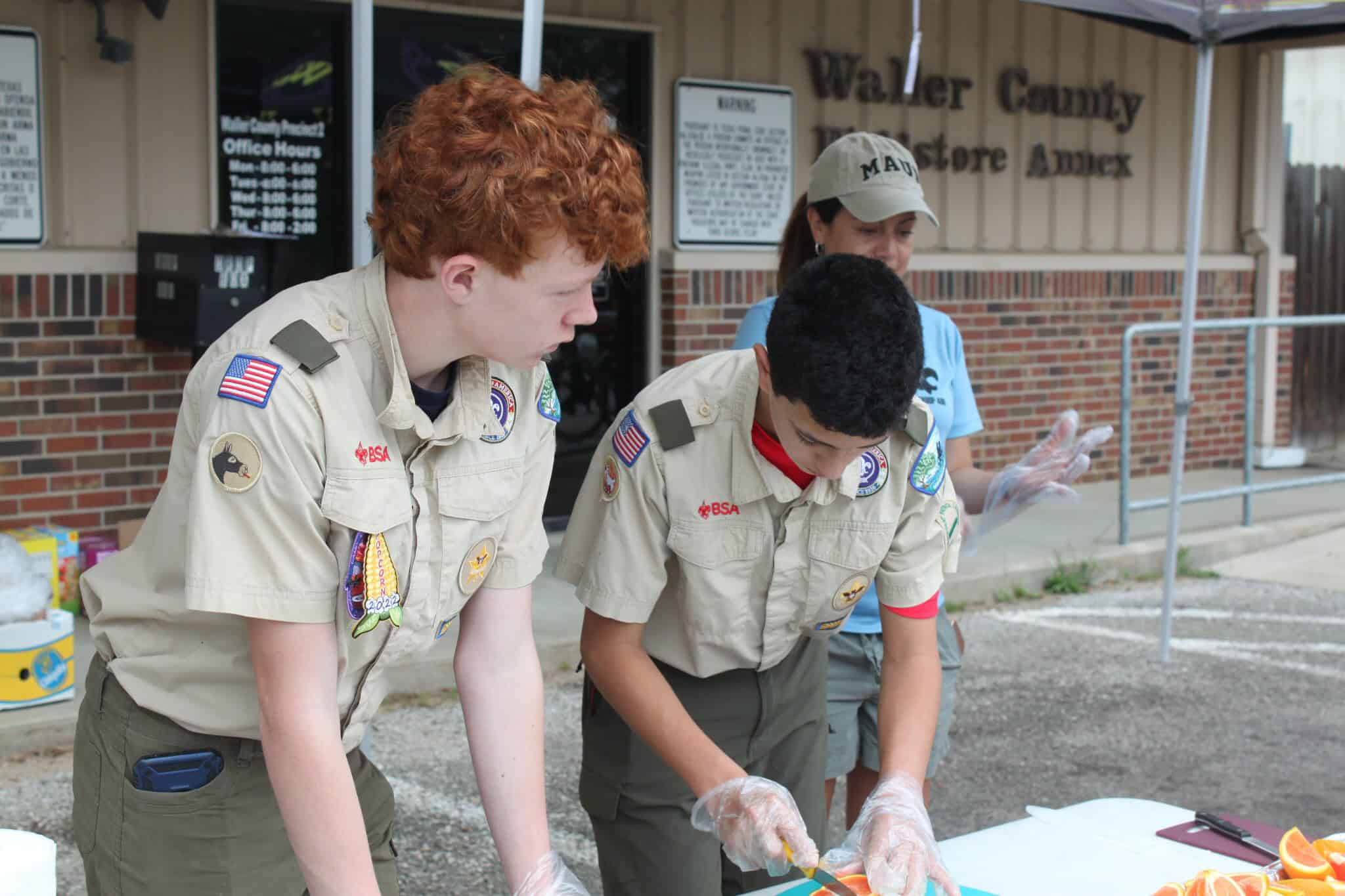 Bright redheaded and young Boy Scout volunteers preparing orange slices outdoors at Bluebonnet Express event.