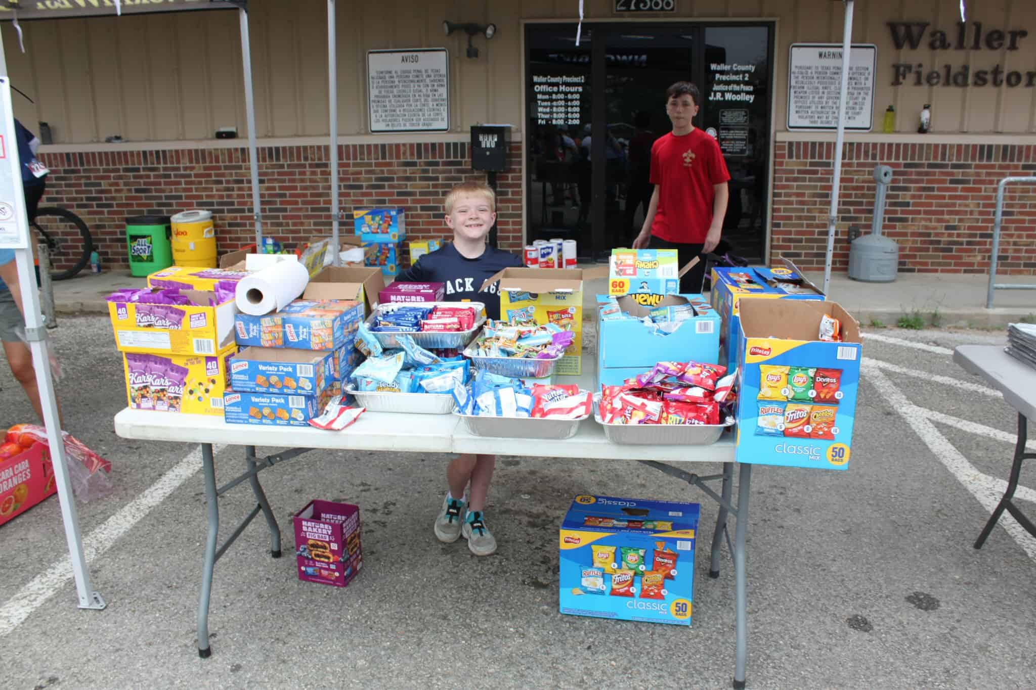 Bright children selling snacks at a community fundraiser event outside the Waller County Precinct building.