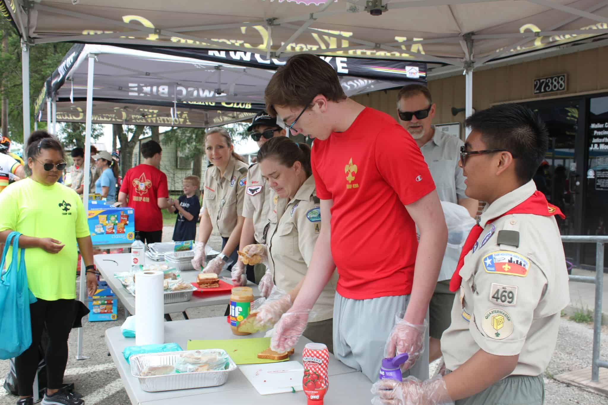 Bright bluebonnet-themed event tent with scouts and community members preparing sandwiches outdoors.