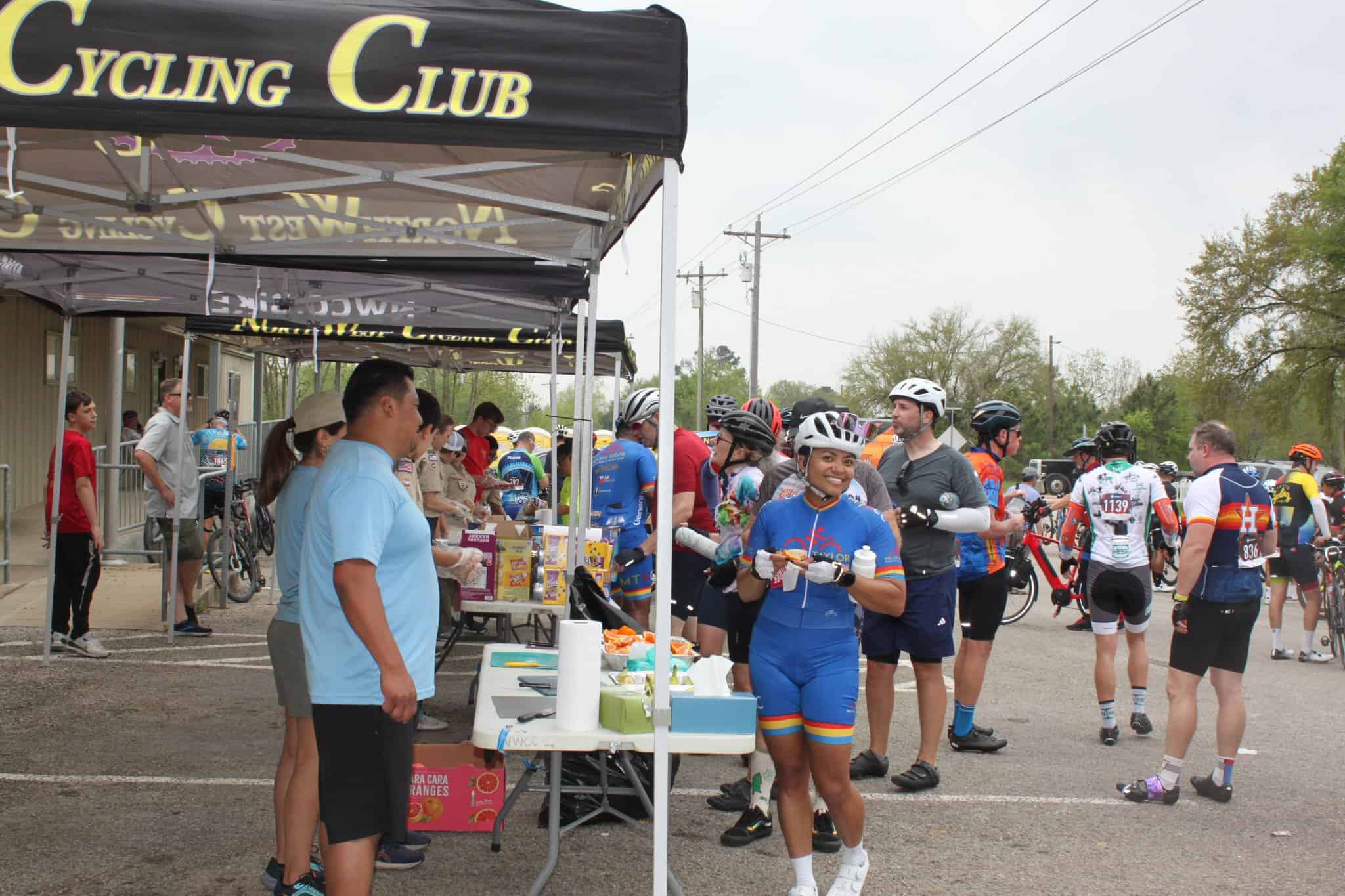 Vibrant cyclist enjoying snack break at Bluebonnet Express Bike Race event, with volunteers and fellow riders.