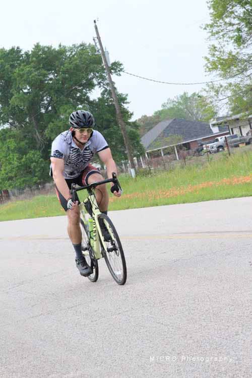 Velo cyclist riding on rural road in helmet and sports gear for Bluebonnet Express race.