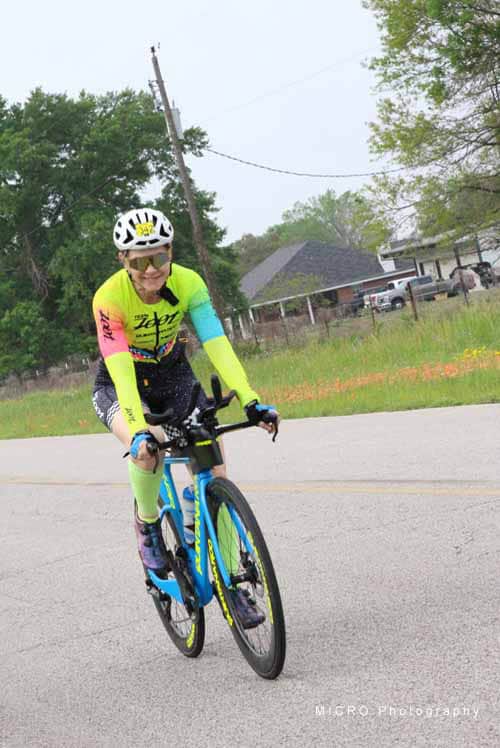 Bright yellow and blue cycling jersey on female cyclist riding on a suburban road.