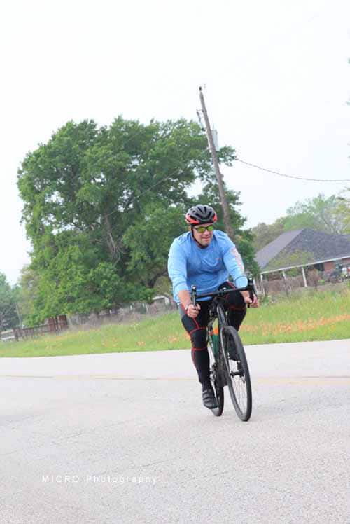 Cyclist riding on the road with greenery in the background, promoting outdoor biking and eco-friendly transportation.