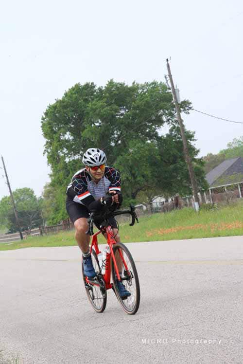 Cyclist riding a bike on a rural road with trees in the background during daytime.