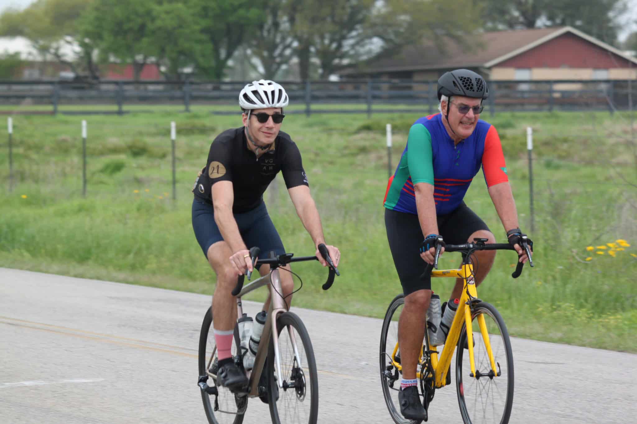 Two cyclists riding on the road during daytime, enjoying outdoor biking activities.