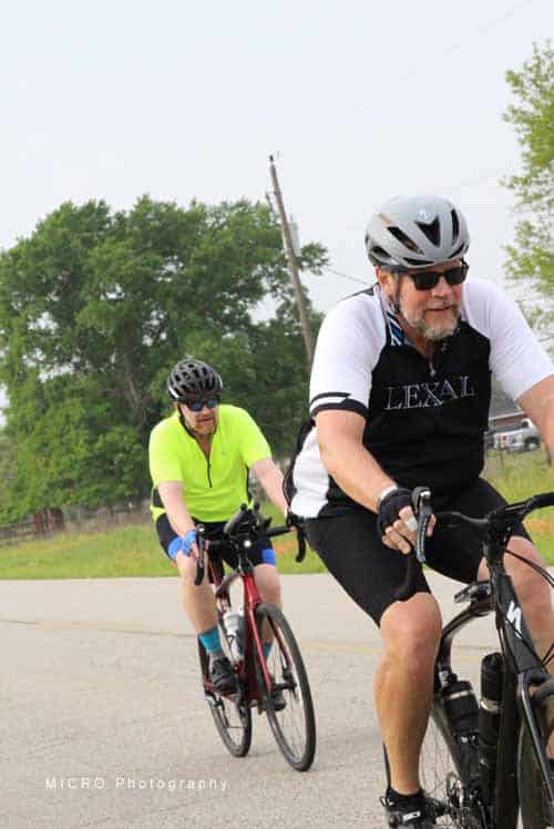 - Man and woman cycling outdoors on scenic rural road with green trees.