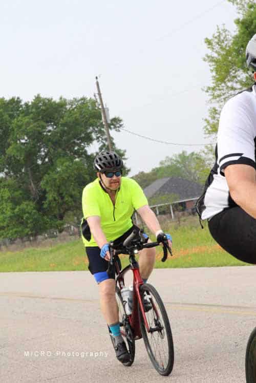 Bright cyclist wearing neon yellow jersey riding bike on open road during daytime.