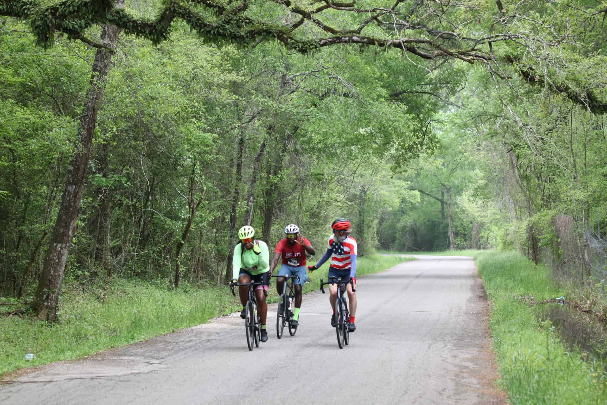 Bicyclists riding through lush green forest on Bluebonnet Express trail, enjoying outdoor cycling.