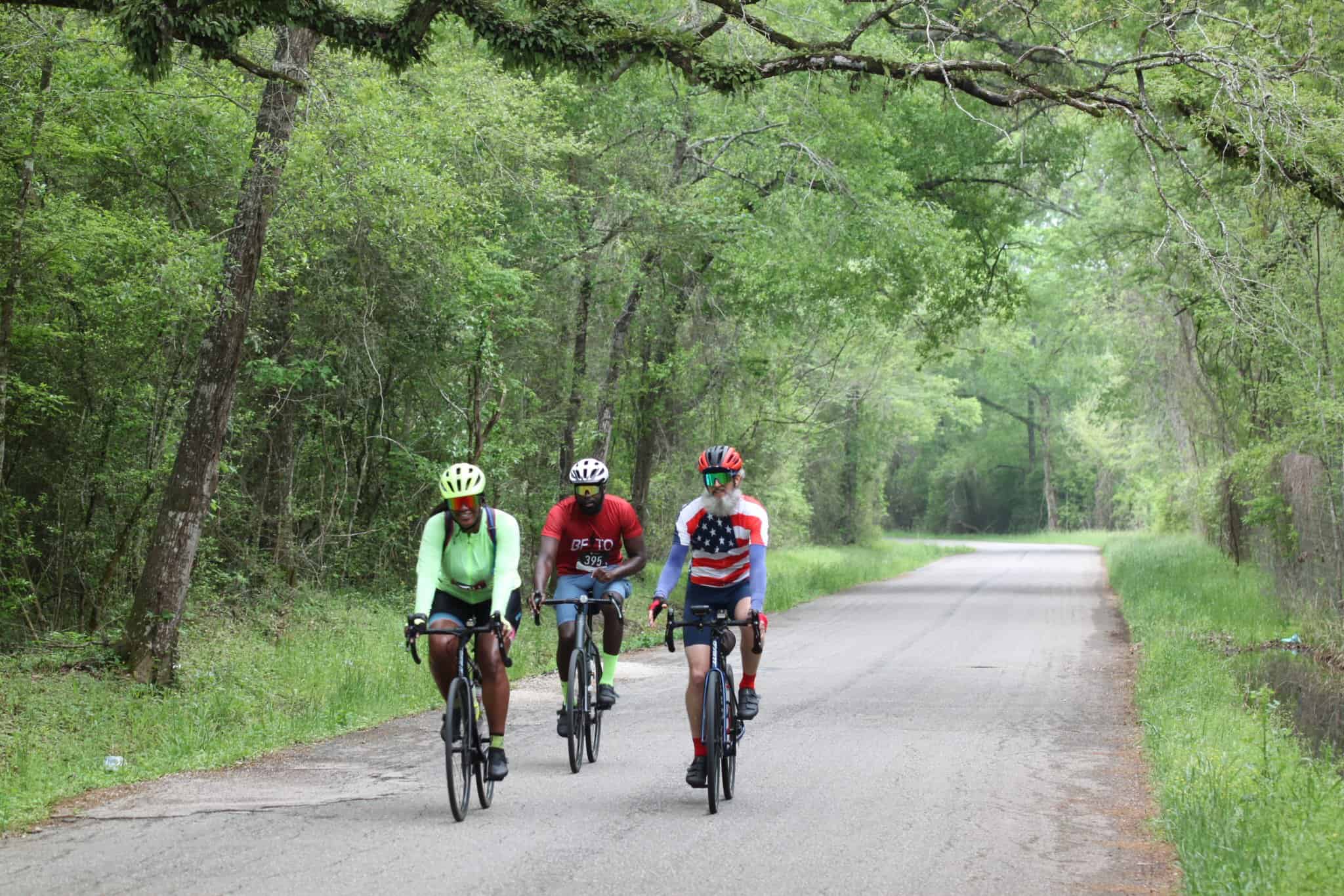Vibrant cyclists riding through lush forest on Bluebonnet Express trail for outdoor biking adventure.