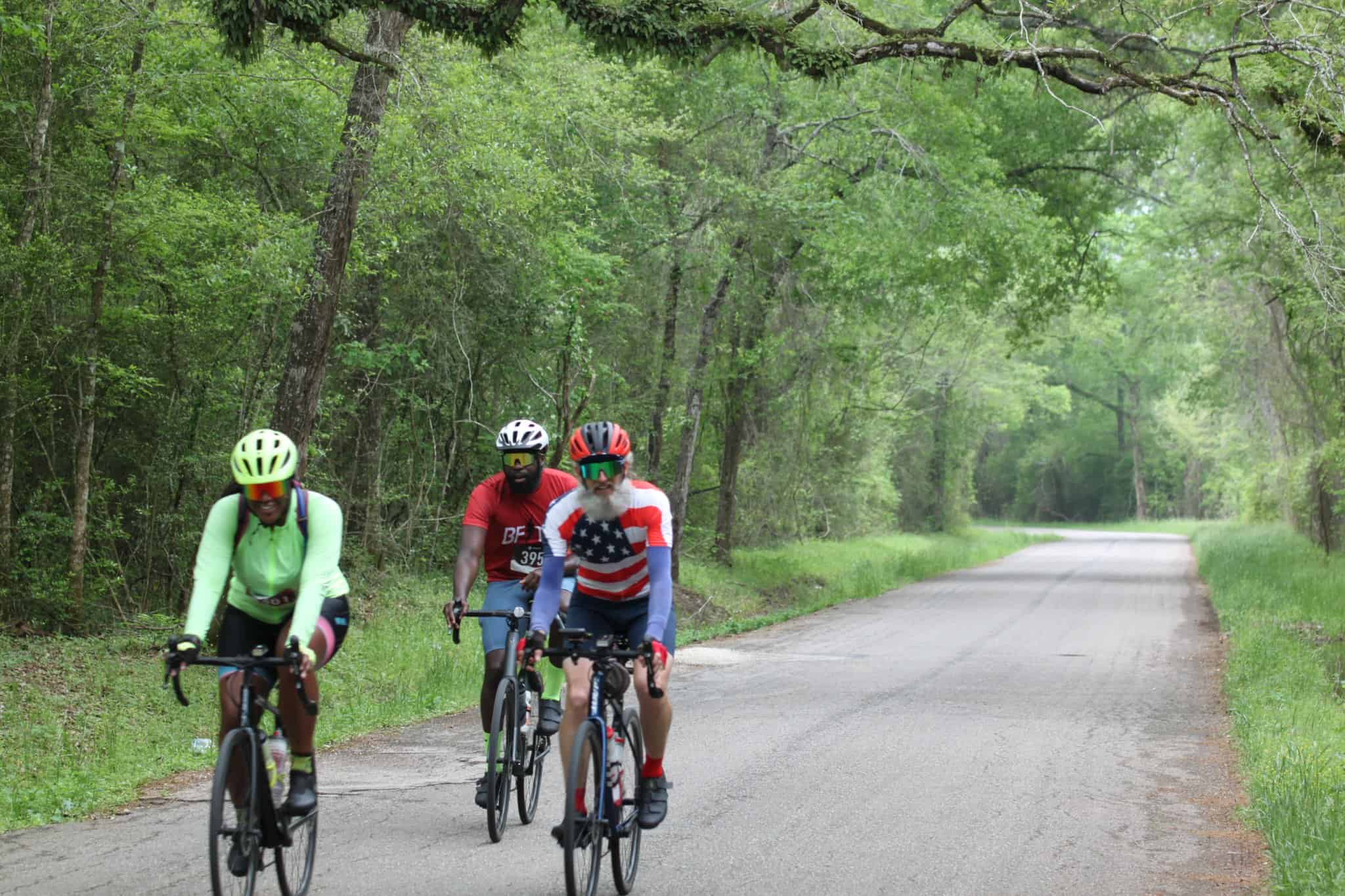 Brightly dressed cyclists riding on a scenic forest bike trail with lush green trees.