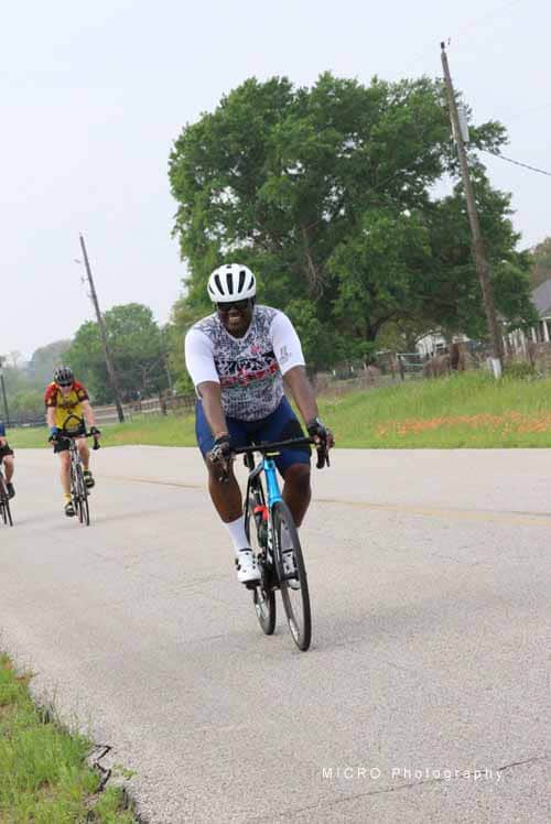 Velo cyclist riding on rural road with greenery in background, promoting outdoor biking and fitness.