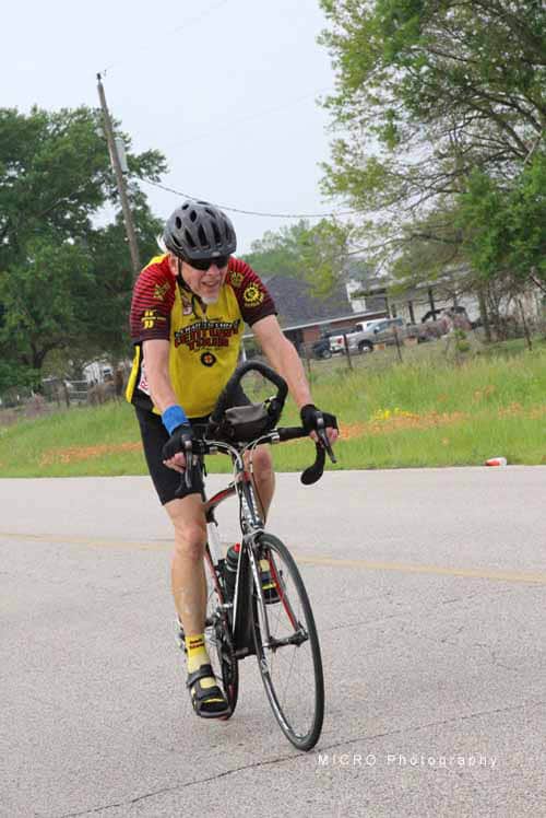 Cyclist wearing a yellow jersey riding a bike on a suburban road for Bluebonnet Express event.