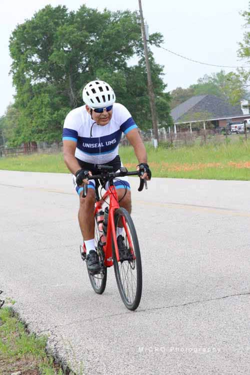 Bright male cyclist wearing white helmet and UNISEAL cycling jersey riding a red bike on a rural road.