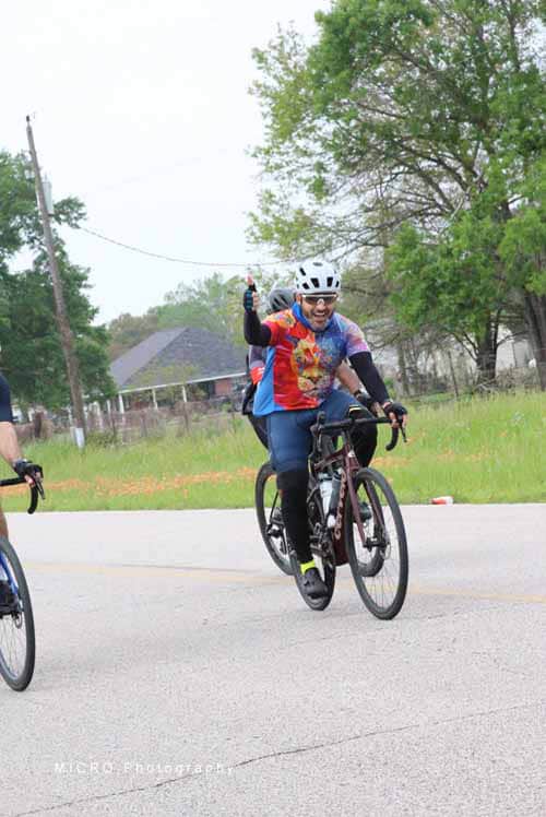 Cyclist smiling and raising fist during Bluebonnet Express event, enjoying a bike ride in Texas.