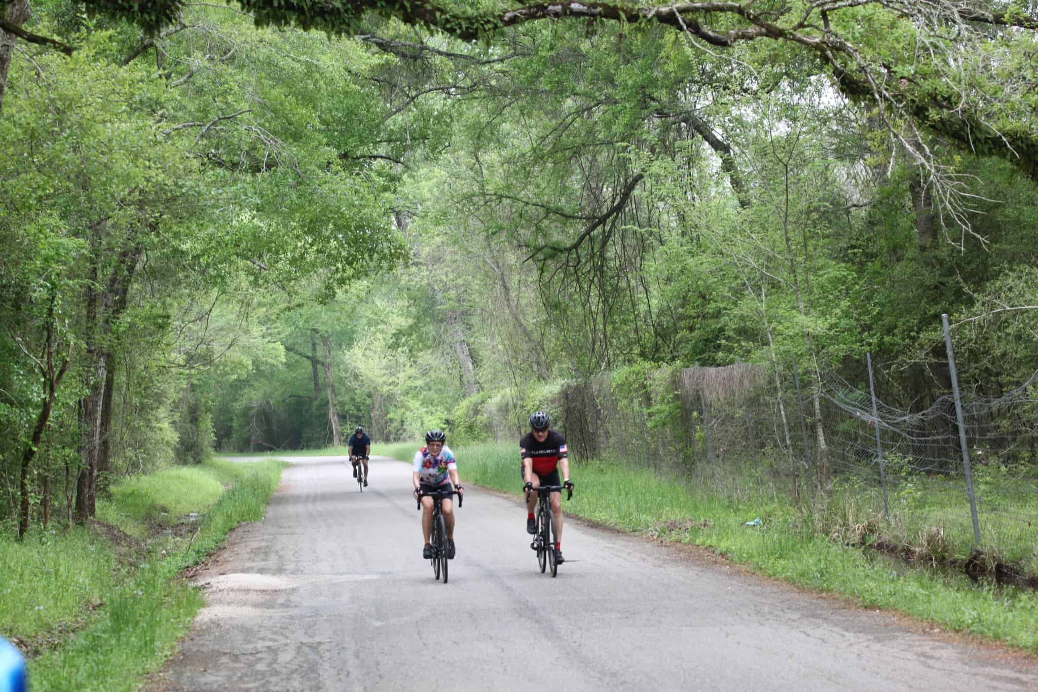 Cyclists enjoying a ride on the scenic Bluebonnet Express bike trail through lush green trees.
