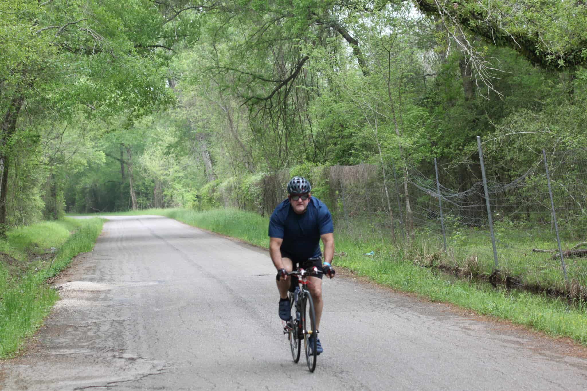 A man cycling on a scenic forested road during daytime, promoting Bluebonnet Express bike tours.