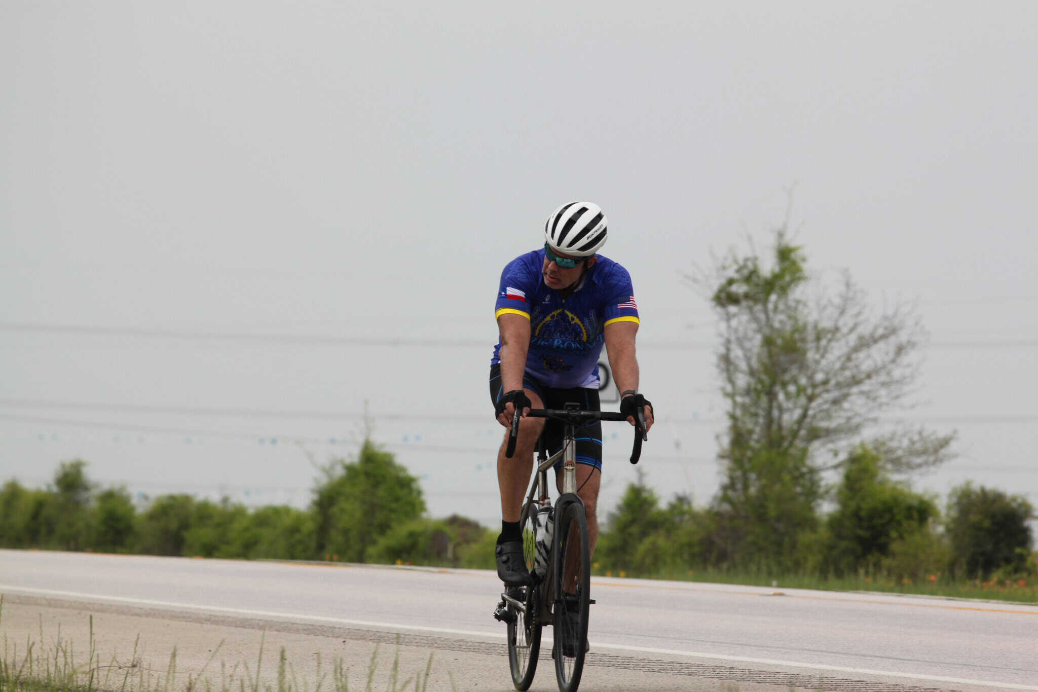 Bike rider in Bluebonnet Express cycling jersey on open road, scenic Texas countryside.