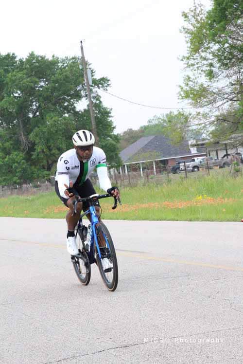 Cyclist riding on the road with greenery, promoting Bluebonnet Express cycling event.