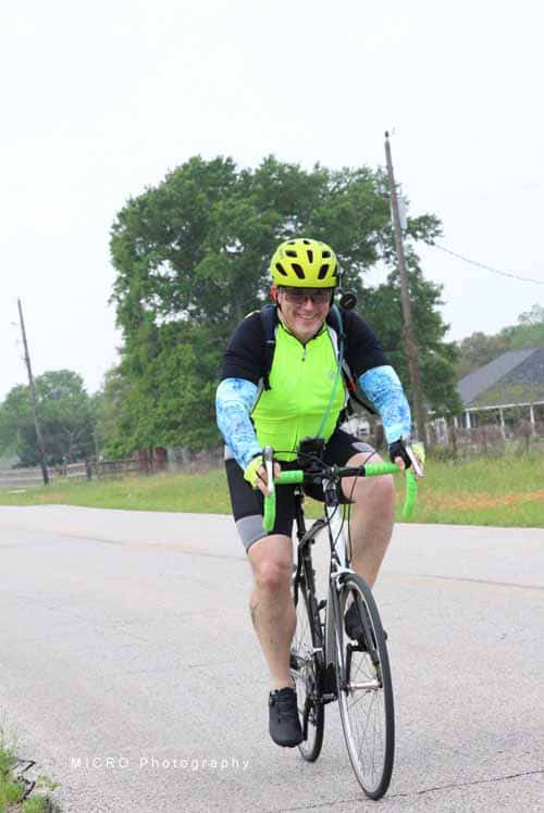 Bright green and yellow cycling helmet with a neon vest on a man riding a bike on rural road.