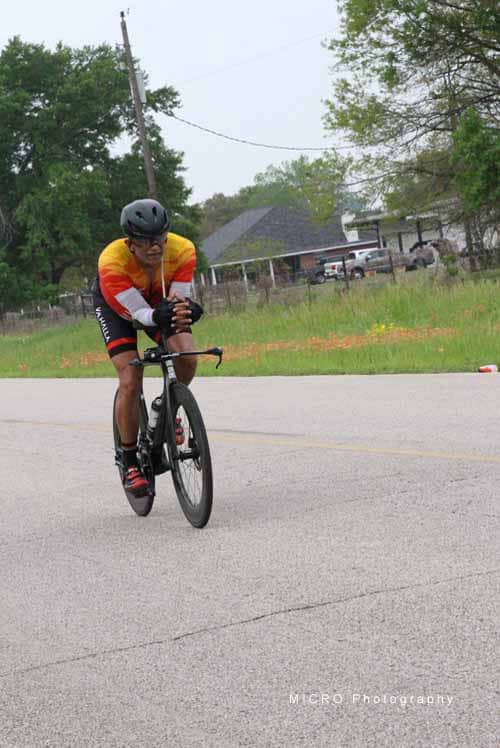 A cyclist riding on the road during daytime, wearing a helmet and colorful cycling gear.
