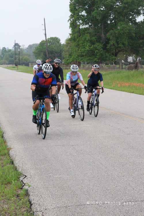 Riders enjoying a group bike ride along a scenic countryside road with green trees.