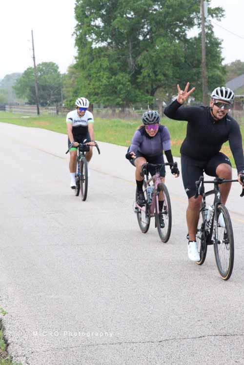 Brightly colored bikers riding along rural road for Bluebonnet Express cycling event.